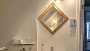 A bathroom with a white sink, dark cabinets, a gold-framed mirror, and a small trash can. - Auberge aux petits oiseaux (BAIE SAINT PAUL)