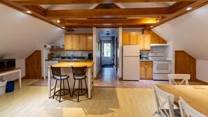 A kitchen with wooden beams, a central island, and a view into a hallway. - Auberge aux petits oiseaux (BAIE SAINT PAUL)