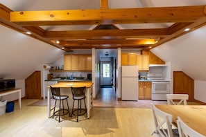A kitchen with wooden beams, a central island, and a view into a hallway. - Auberge aux petits oiseaux (BAIE SAINT PAUL)