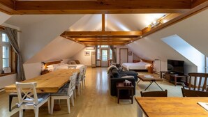 A spacious loft with a high ceiling, wooden beams, a dining area, a sofa, a TV, and a fireplace. - Auberge aux petits oiseaux (BAIE SAINT PAUL)