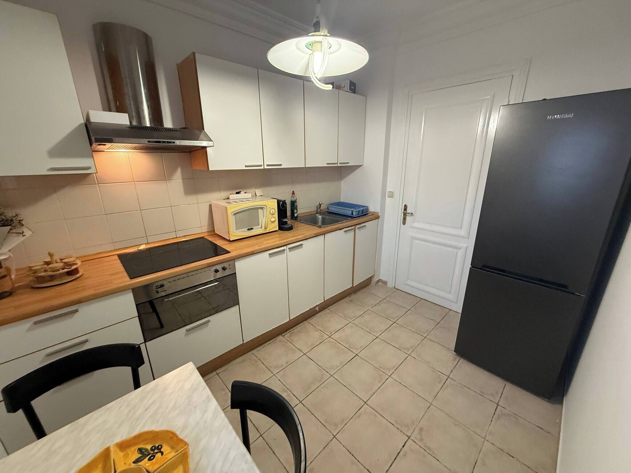 Een kleine keuken met witte kastjes, een zwarte koelkast, een magnetron en een fornuis.