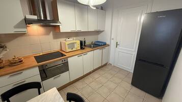 Een kleine keuken met witte kastjes, een zwarte koelkast, een magnetron en een fornuis.