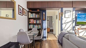 Un saló modern amb un sofà, una taula de dinar amb cadires, una biblioteca i un gran mirall.