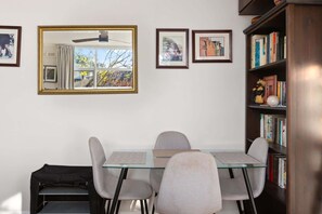 A dining area with a glass table, four chairs, a ceiling fan, and a bookshelf with books and decorative items. - Peaceful Hideaway 2-Bed Apartment Mosman (Mosman)