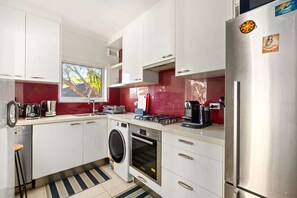 A compact kitchen with white cabinets, a washing machine, a stove, and a refrigerator. - Peaceful Hideaway 2-Bed Apartment Mosman (Mosman)