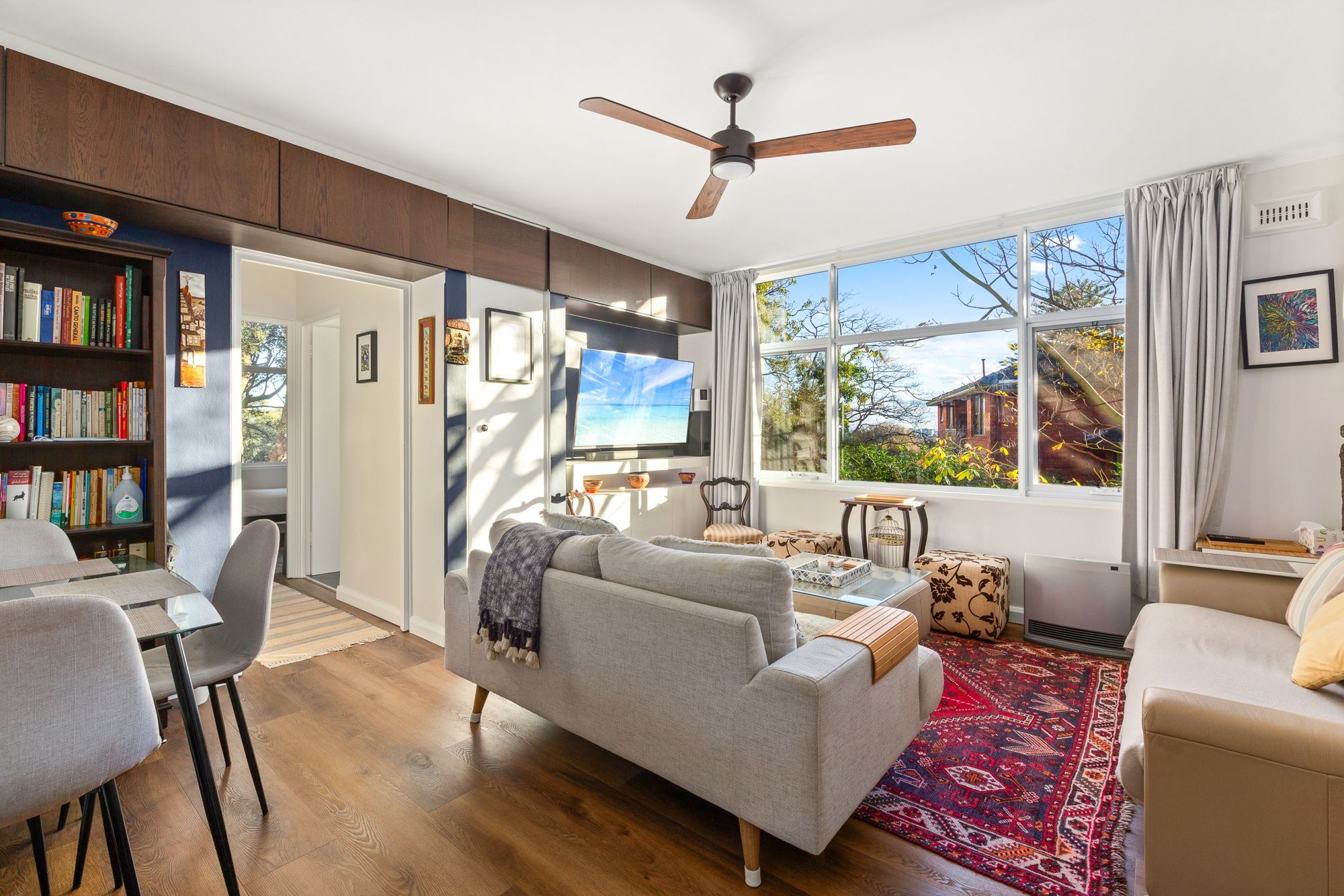 A modern living room with a sofa, armchairs, a coffee table, a bookshelf, and a large window with a view.