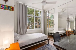 A bedroom with a bed, a desk, and a chair. There is a window with curtains, a ceiling fan, and a door with a mirror. - Peaceful Hideaway 2-Bed Apartment Mosman (Mosman)