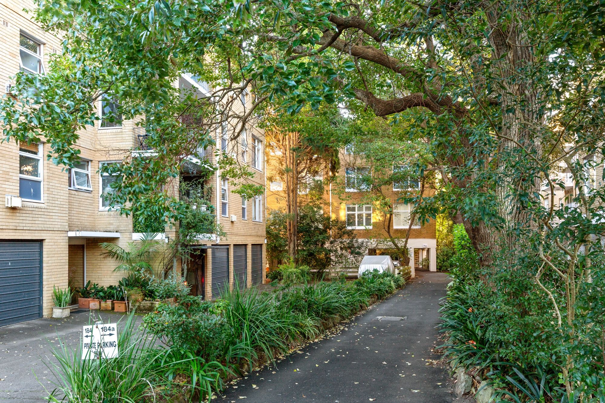 A narrow alleyway flanked by residential buildings with a covered car parked on the right.