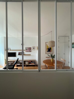 A modern living room with a dining area, a bookshelf, and a television. - Le Congrès - Cozy apartment 50 meters from the beach (Royan)