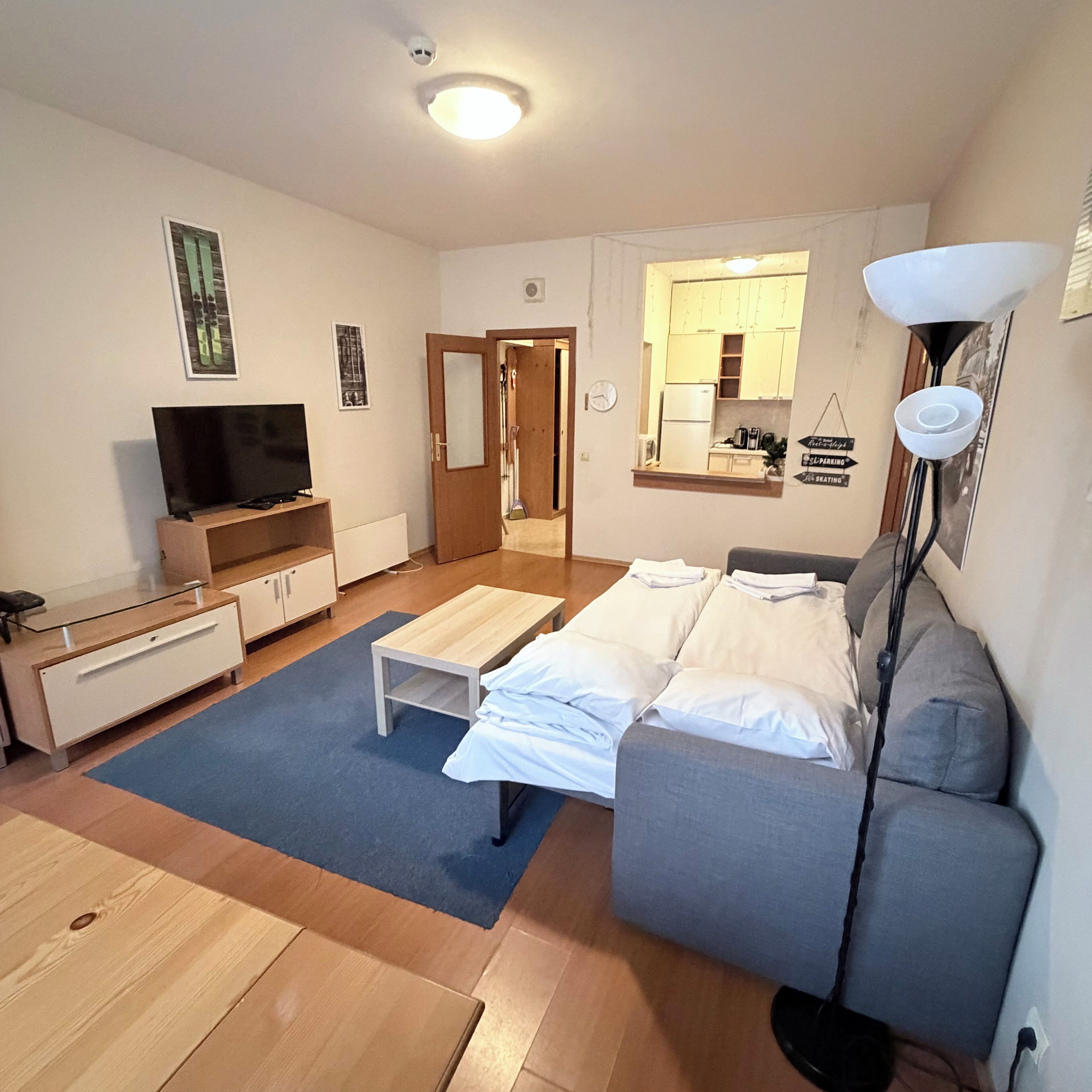 Un espacio habitable compacto con sofá, televisor, kitchenette pequeña y una puerta que conduce a otra habitación.