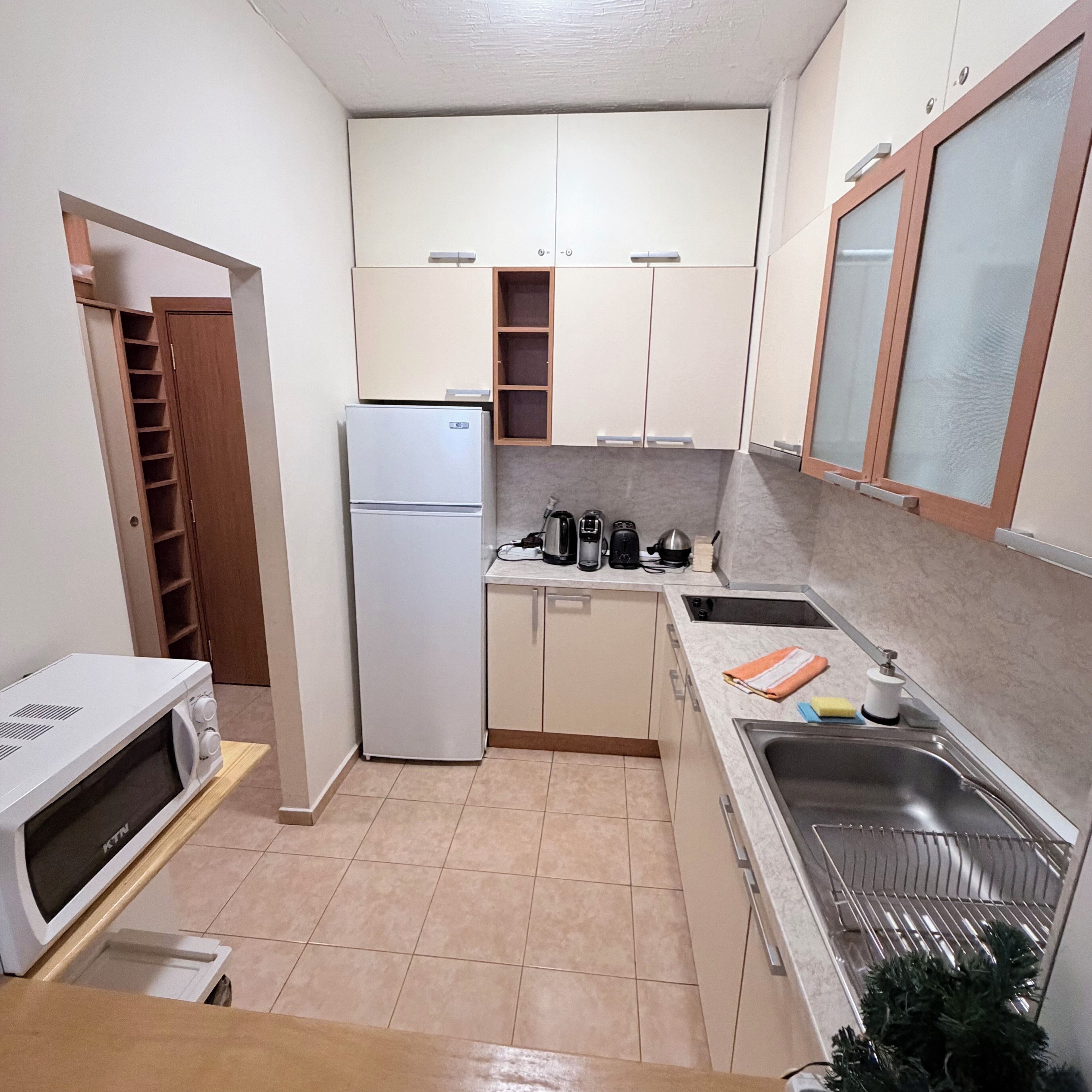 Cocina compacta con refrigerador, microondas, pileta y una mesada pequeña con hervidor y tostadora.