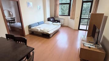 Una habitación con cama, escritorio, silla, televisión y ventana con cortinas.