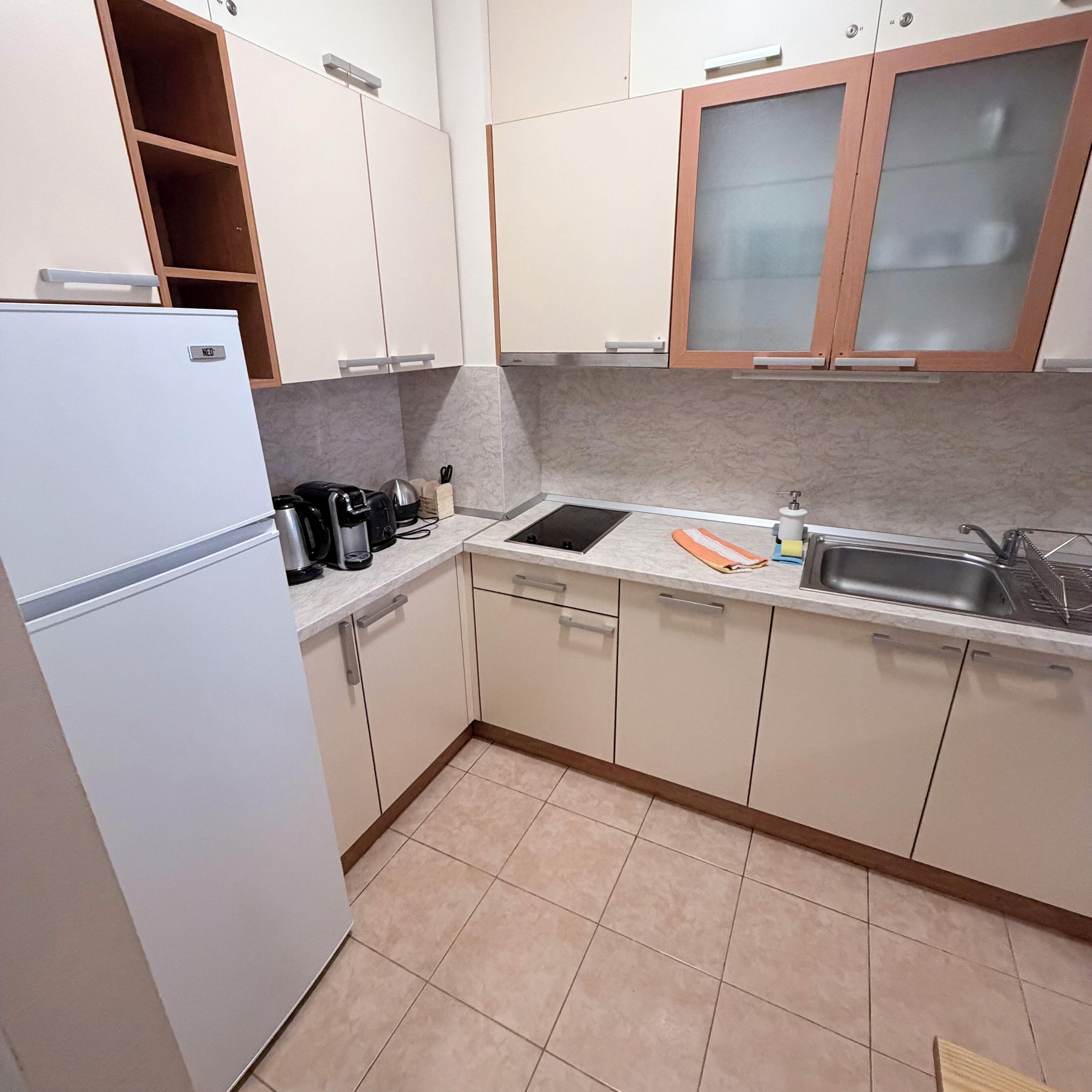Una cocina con armarios blancos, horno empotrado, lavabo y encimera con tetera y cafetera.