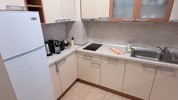 Una cocina con armarios blancos, horno empotrado, lavabo y encimera con tetera y cafetera.