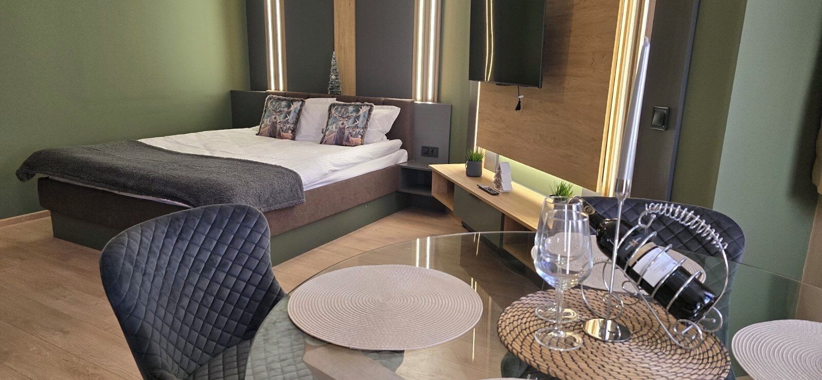 A modern hotel room with a bed, a seating area with a table, and a TV mounted on the wall.