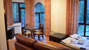 Una habitación con una cama, una mesa, sillas, un televisor y ventanas grandes con cortinas.