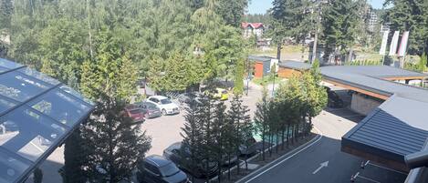 Un estacionamiento con varios autos, un edificio de techo rojo y un fondo boscoso.