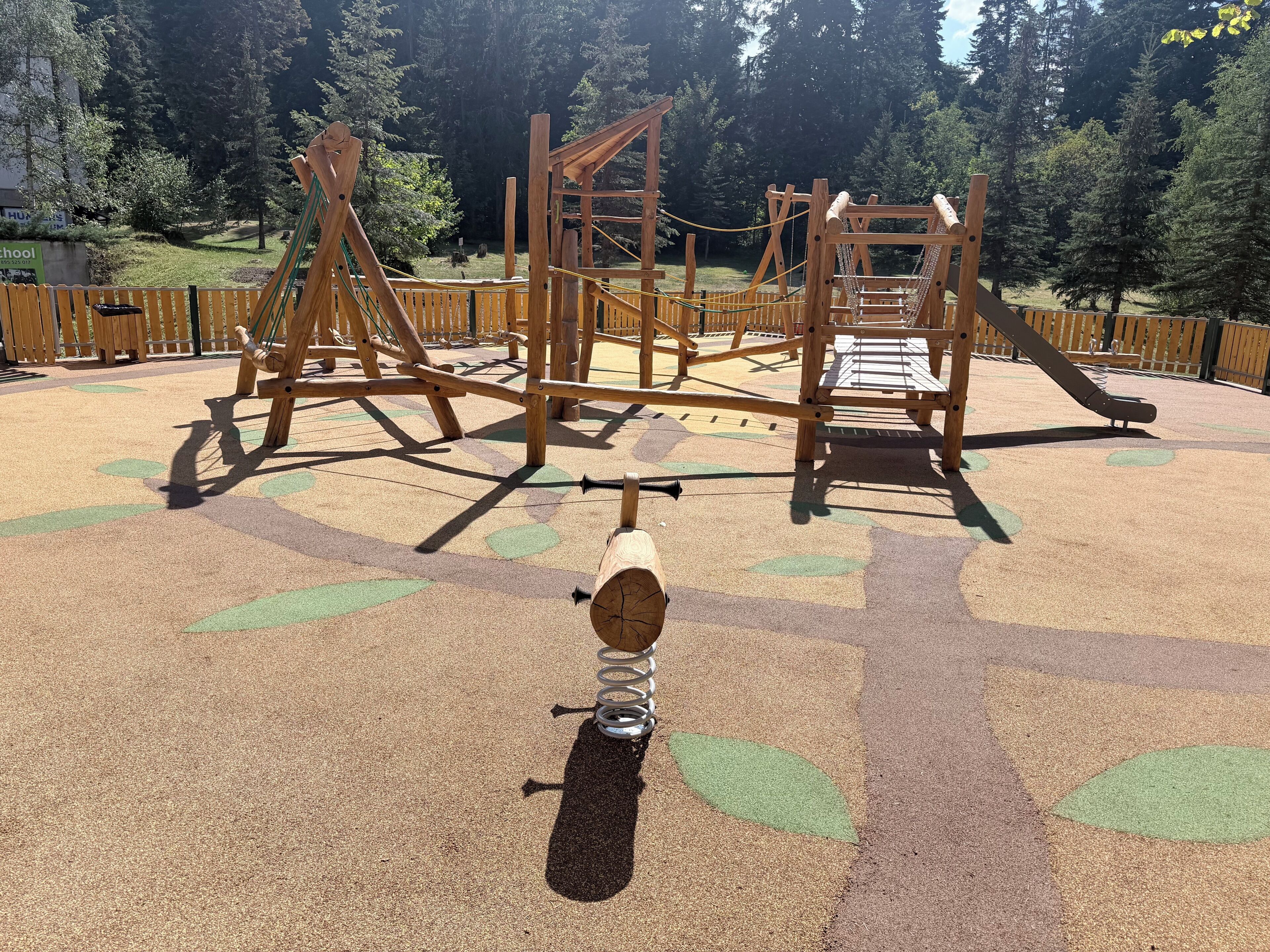 Un parque infantil con diversas estructuras de madera para escalar y un suelo suave con diseño.