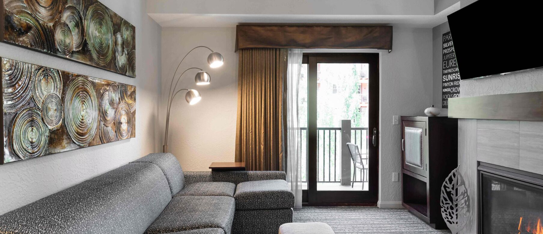 Un salon moderne avec un canapé gris, une lampe sur pied et une cheminée.