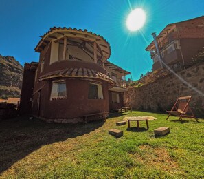 Un edifici rústic amb una estructura circular, un petit pati amb taula i bancs, i un cel blau clar.