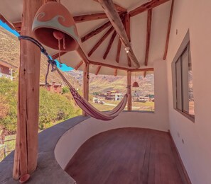 A room with a wooden floor, a hammock, and a view of a mountainous landscape.