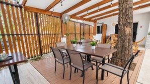 En udendørs patio med et træbord og stole, et receptionsområde og et træ.