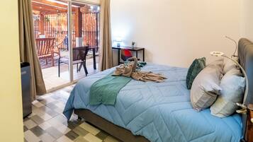 A bedroom with a bed, a chair, a table, and a view of an outdoor area with a wooden deck and chairs.