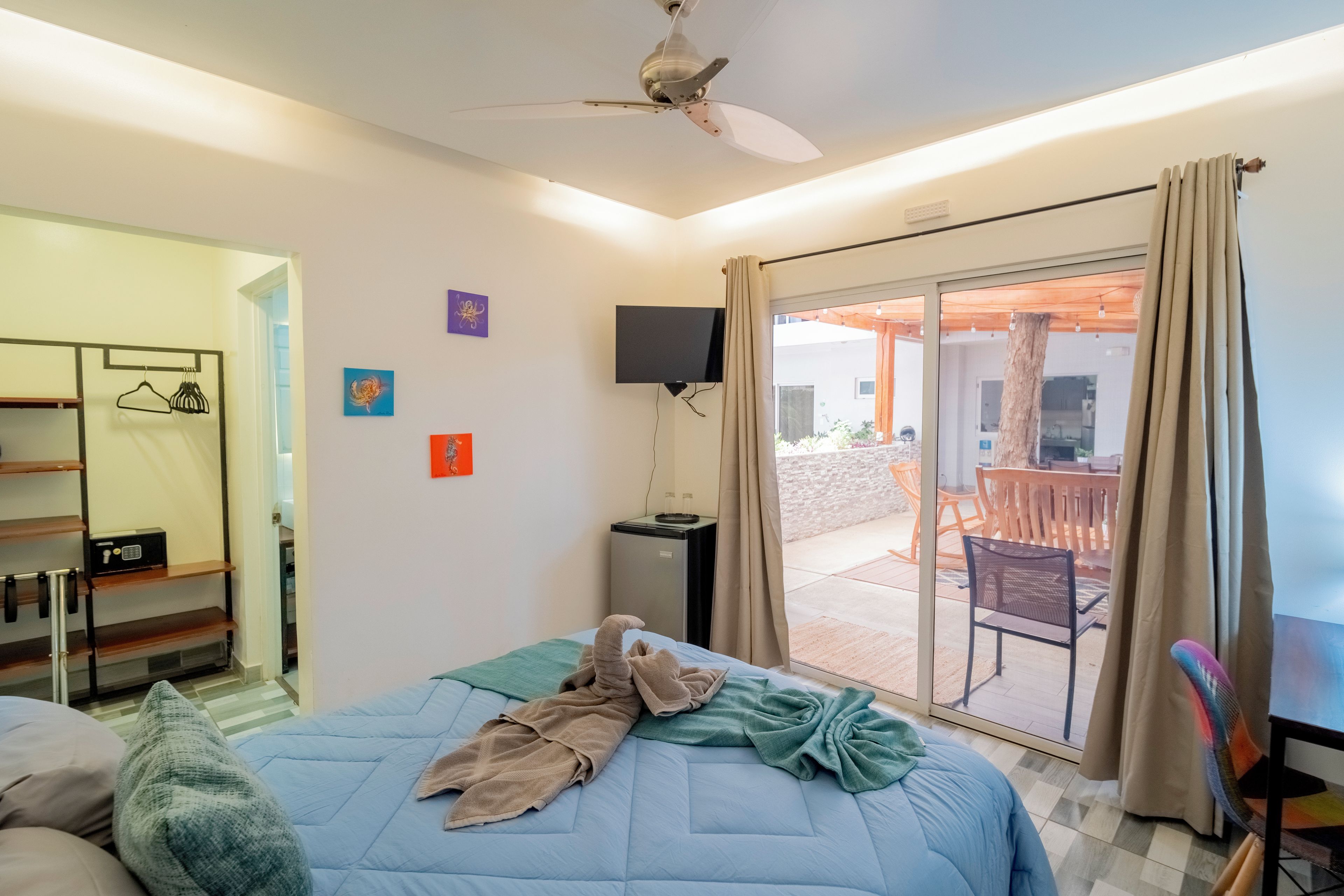 Habitación de hotel con cama, televisión, ventilador de techo y vistas al exterior.