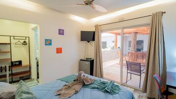 Habitación de hotel con cama, televisión, ventilador de techo y vistas al exterior.