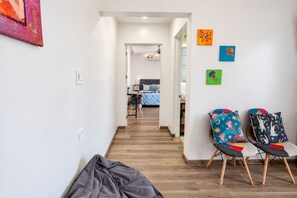 Un corridoio che conduce a una camera da letto con un letto, una sedia con cuscini colorati e opere d'arte appese alle pareti.
