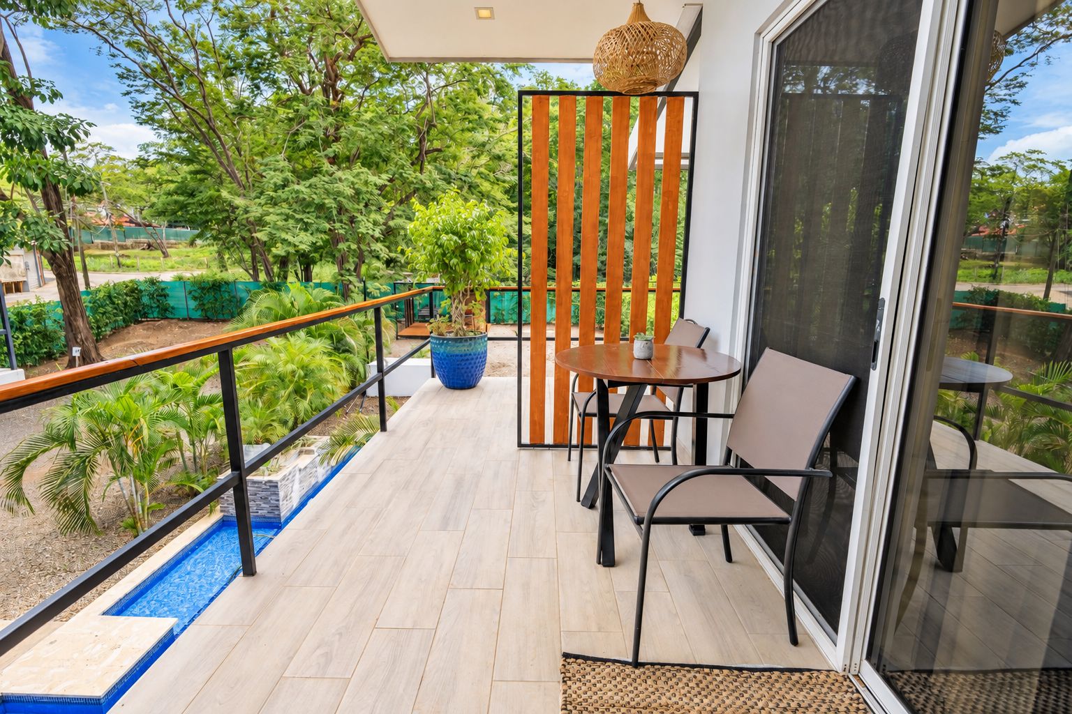 A balcony with a table and chairs, a potted plant, and a view of greenery.