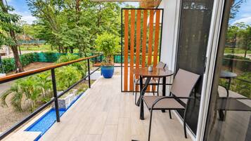 A balcony with a table and chairs, a potted plant, and a view of greenery.