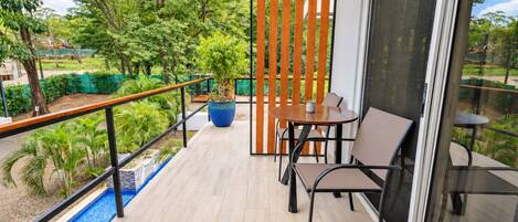 A balcony with a table and chairs, a potted plant, and a view of greenery.