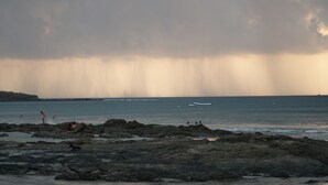 A rocky beach with waves, a boat, and a distant shoreline.