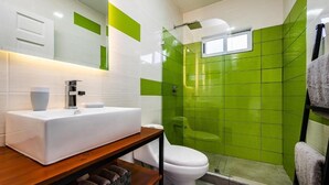 A bathroom with a white sink, a toilet, and a shower area with green tiles.