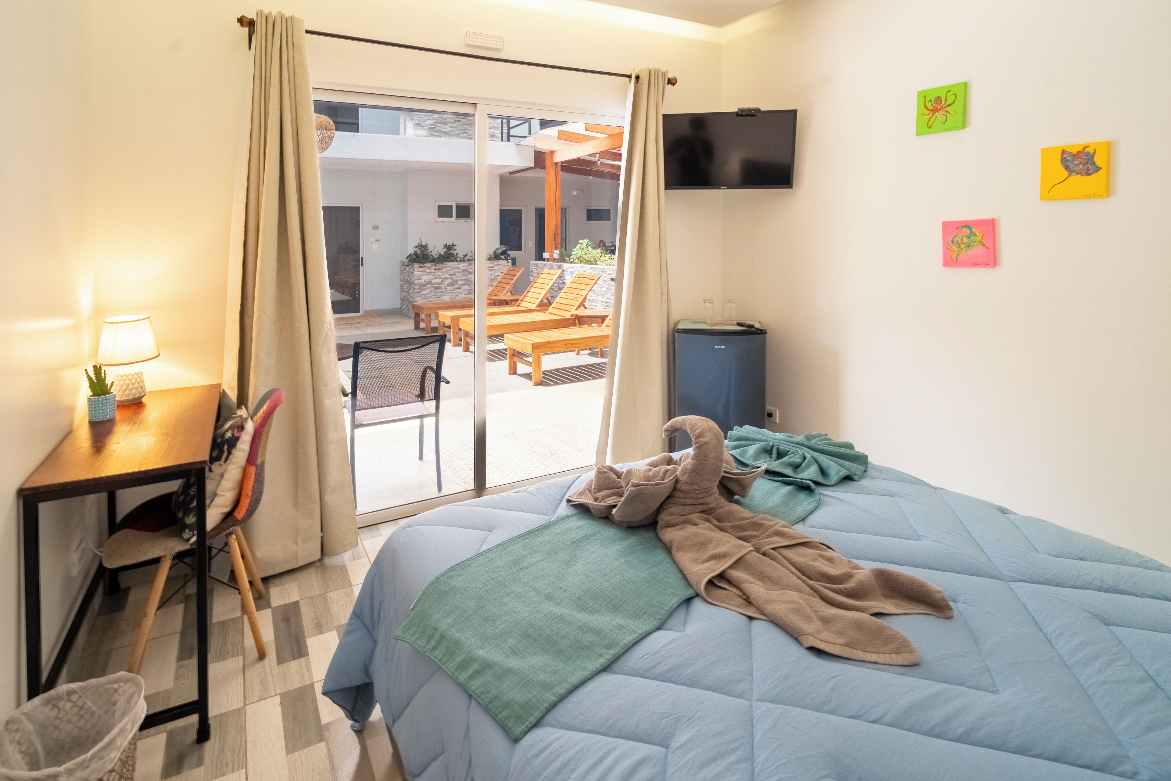 Habitación de hotel con cama, escritorio, silla, televisor y vista al exterior.