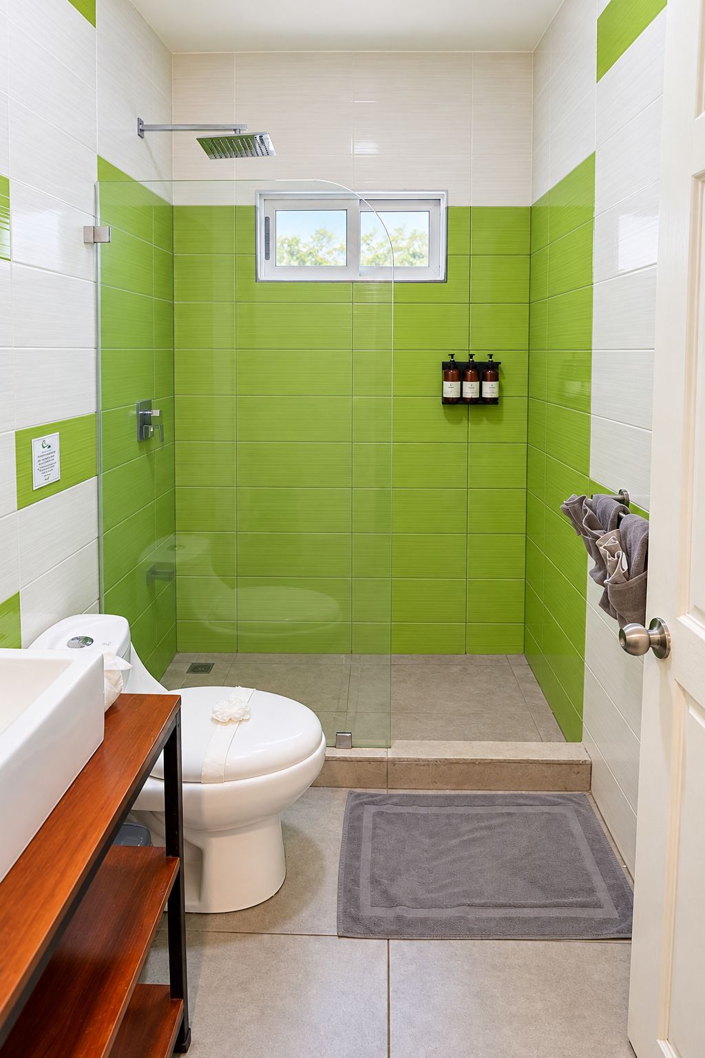 A bathroom with green tiles, a white toilet, a wooden vanity, and a shower area.