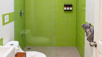 A bathroom with green tiles, a white toilet, a wooden vanity, and a shower area.