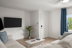 Ein modernes Wohnzimmer mit Fernseher, einer Zimmerpflanze, einem weißen Couchtisch und einem Sofa.