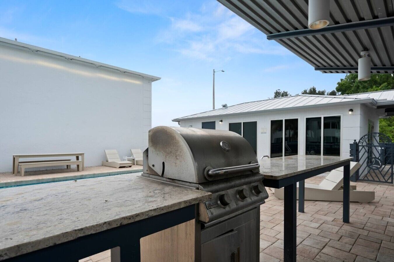 An outdoor patio with a barbecue grill, a pool, and a covered seating area.