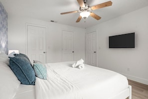 Ein Schlafzimmer mit einem Bett, einem Deckenventilator und einem an der Wand befestigten Flachbildfernseher.