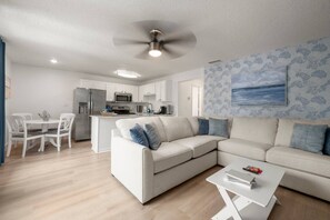Ein modernes Wohnzimmer mit Sofa, Couchtisch und Blick auf die Küche im Hintergrund.