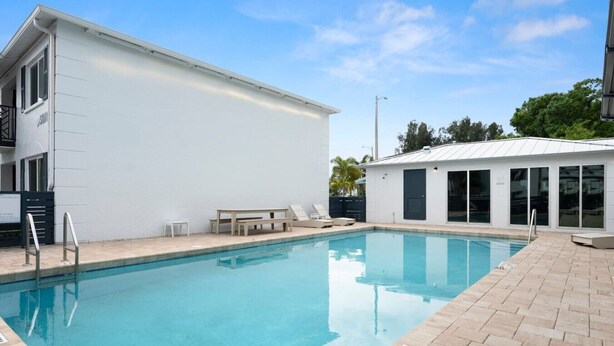 A swimming pool with a white building adjacent to it, a small table, and a bench.