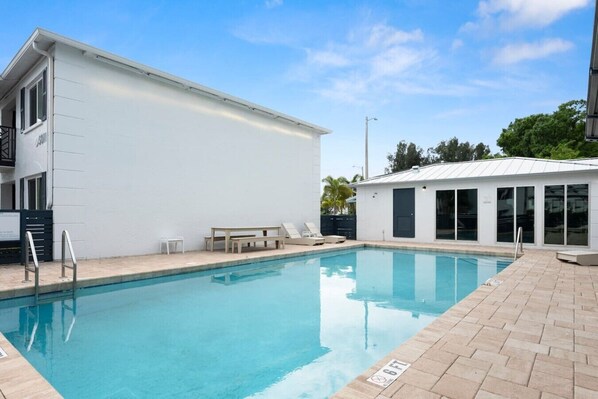 A swimming pool with a white building adjacent to it, a small table, and a bench.