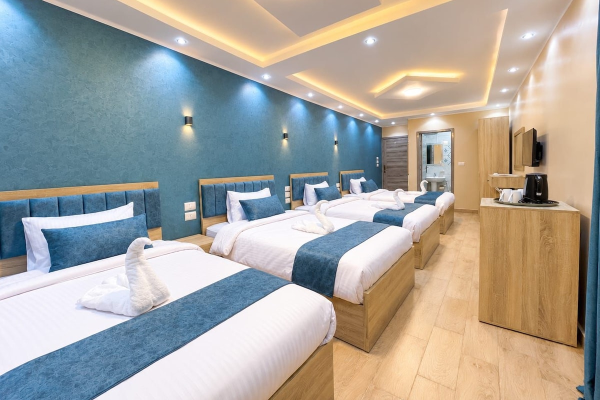 A hotel room with four beds arranged in a row, a wooden cabinet, and a mirror on the wall.