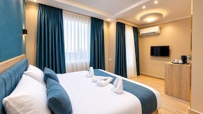 A hotel room with a bed, a television, a desk, and a window with curtains.