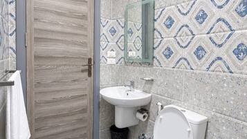 A bathroom with a wooden door, a sink, a toilet, and a mirror on the wall.