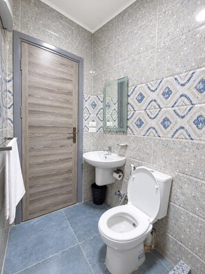 A bathroom with a wooden door, a sink, a toilet, and a mirror on the wall.