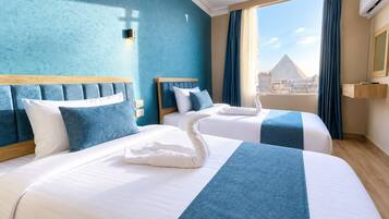 Habitación de hotel con dos camas, un ventanal con cortinas y vistas a la ciudad.