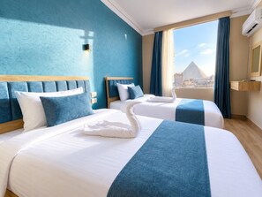 A hotel room with two beds, a large window with curtains, and a view of the city.